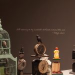 Photograph of an art installation showing birds, clocks, and bird cages