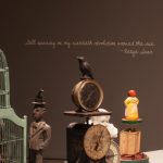 Photograph of an art installation showing birds, clocks, and bird cages