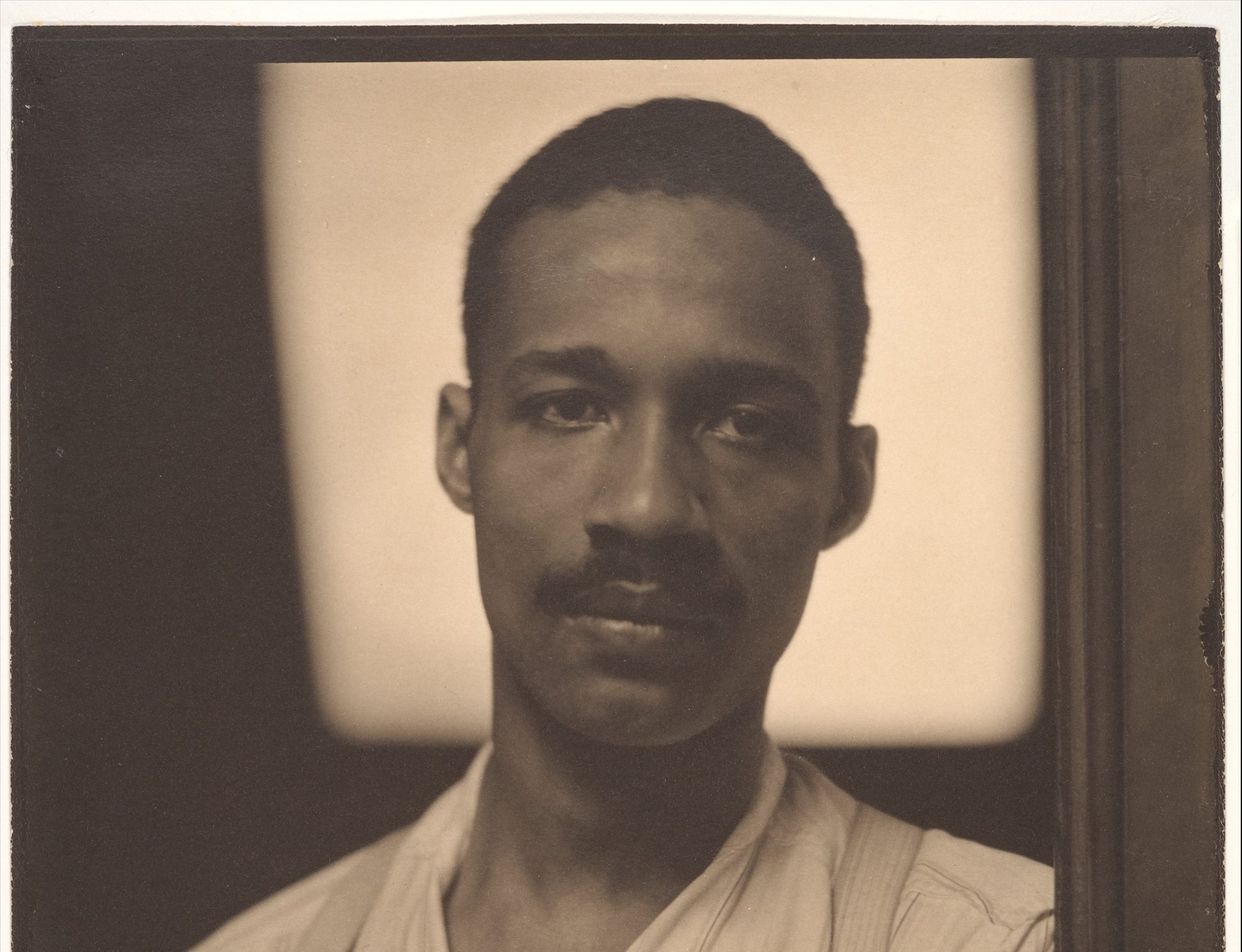 Image of a black man with a mustache wearing a white shirt