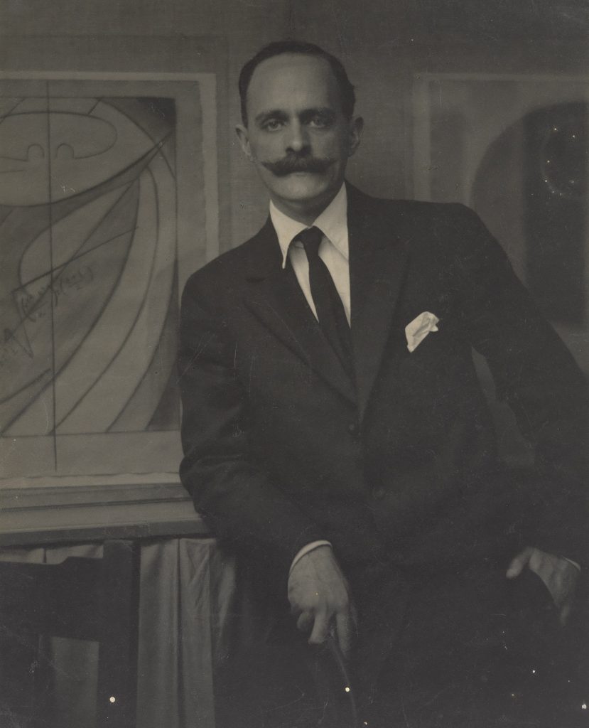Photograph of a white man with a mustache wearing a suit