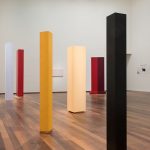 art installation of 6 colored pillars around the room in the colors black, yellow, red, and white