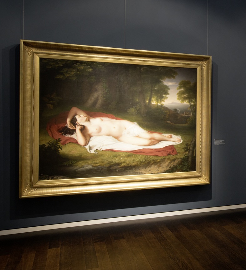 Photo of a painting showing a nude woman laying in the woods