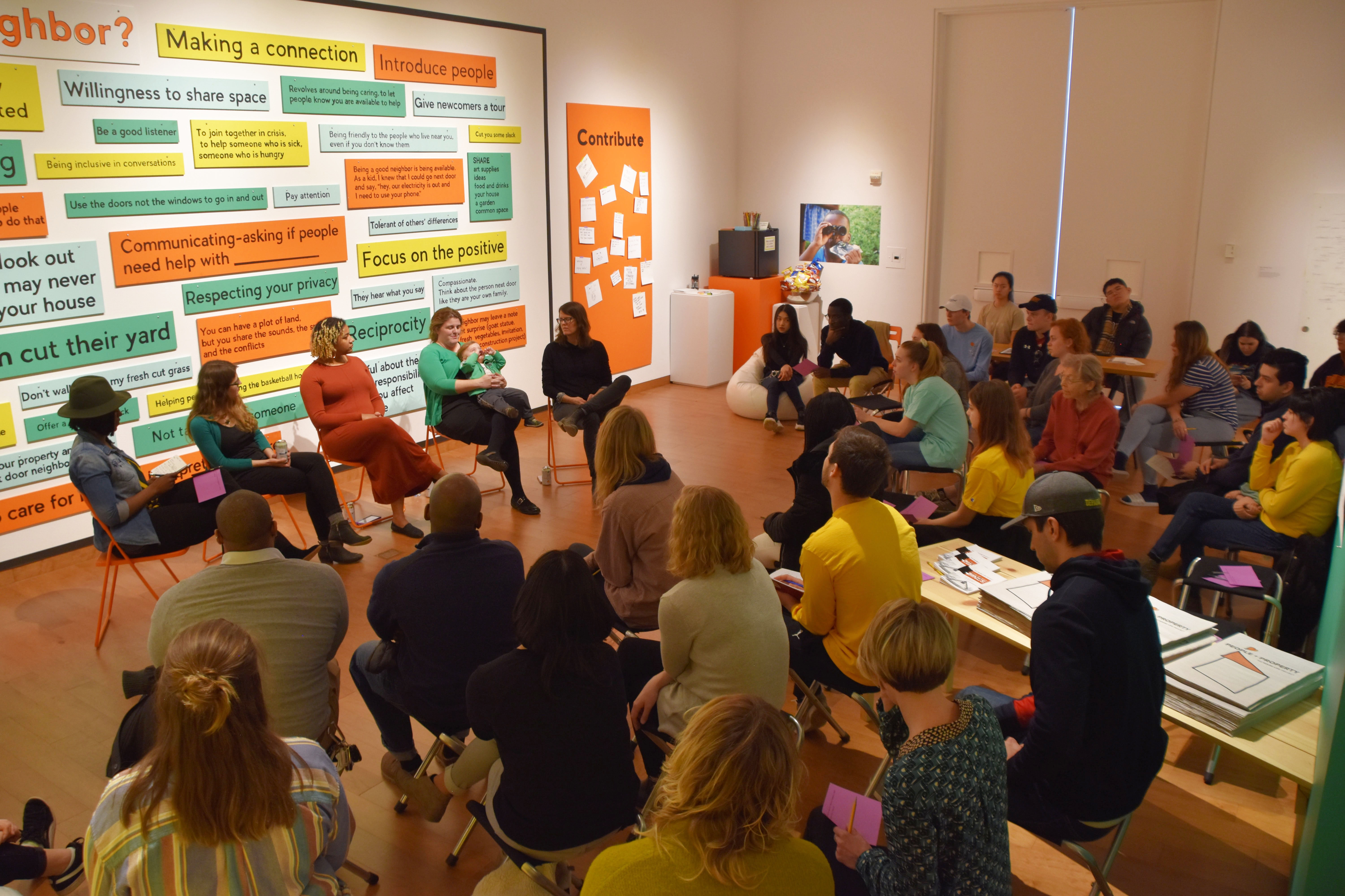 Image of a large group of people attending a talk given by 5 women