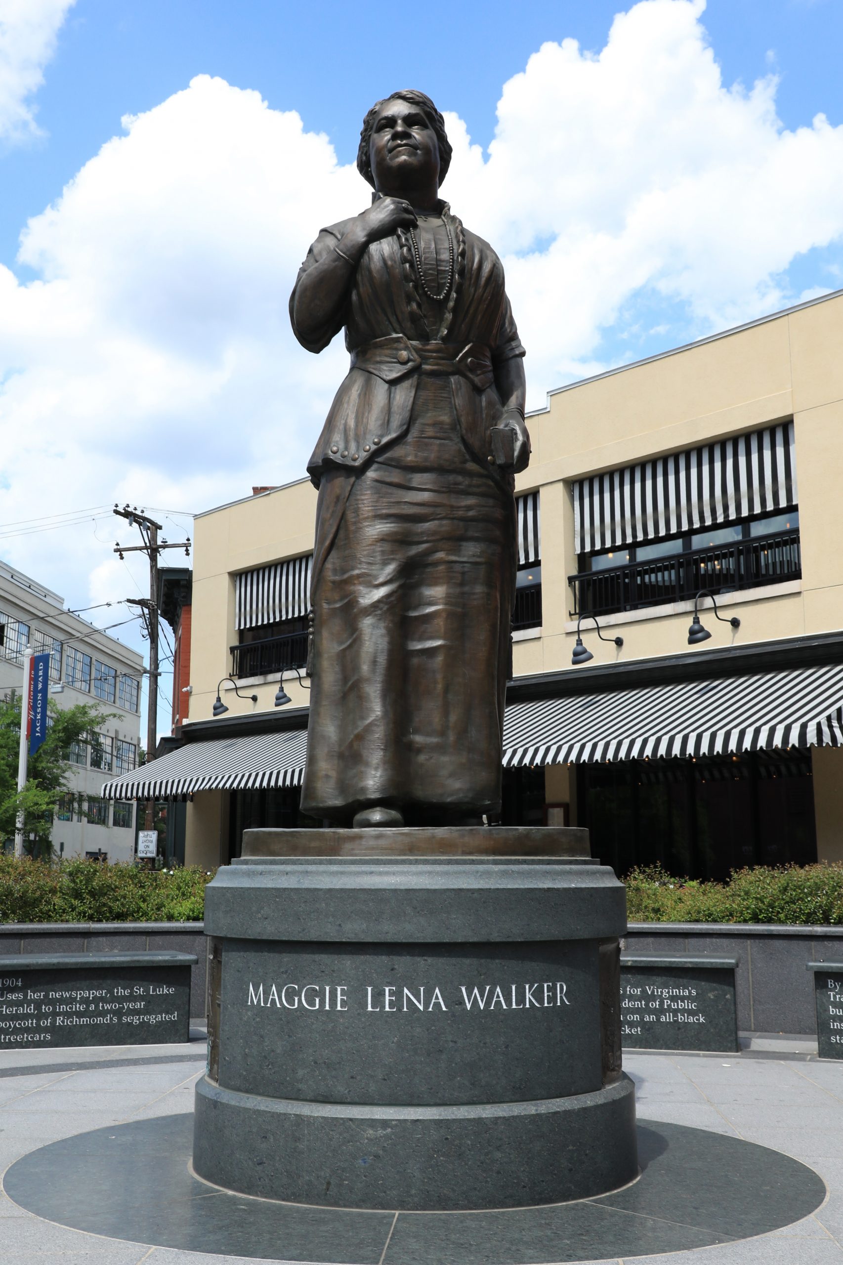 Bronze outdoor statue of a woman in a long skirt on a pedestal that reads MAGGIE LENA WALKER