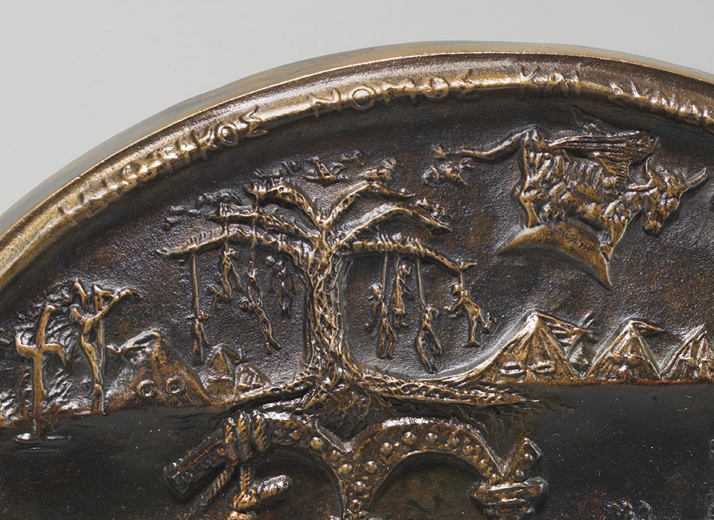 Detail of circular bronze medal featuring lynched figures hanging from a tree.
