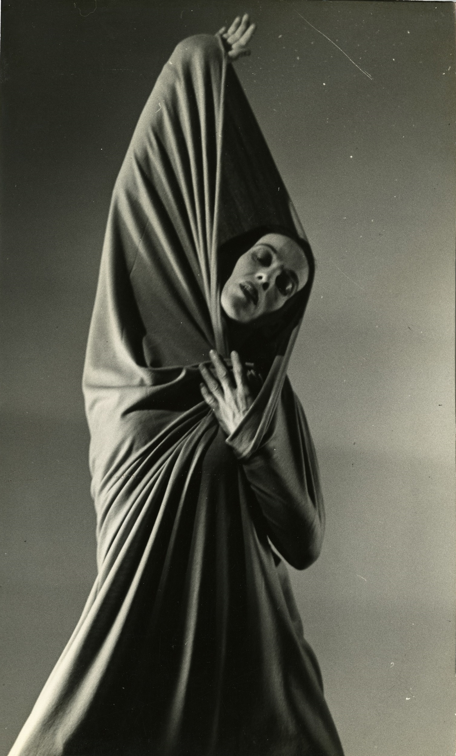 Black and white photograph of a female dancer, one arm over her head holding a scarf that wraps around her body