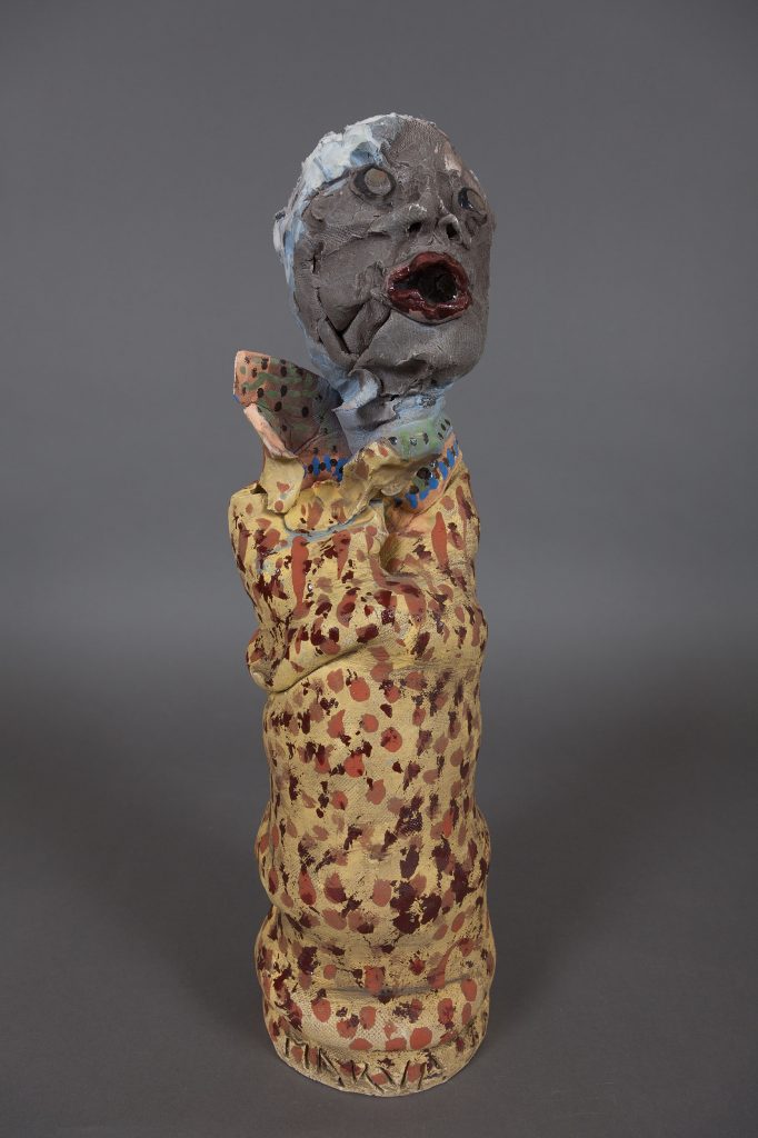 ceramic sculpture with a speckled base and a face-shaped finial.