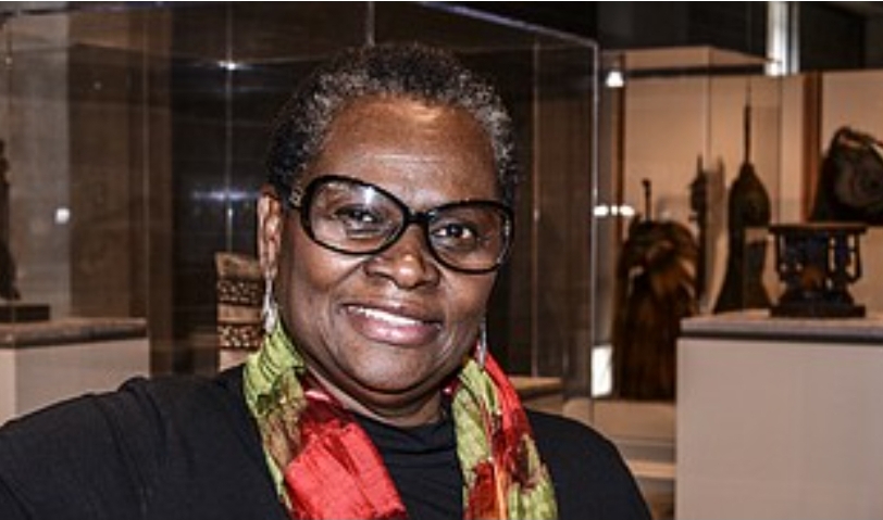 Photograph of a Black woman wearing a colorful scarf and glasses