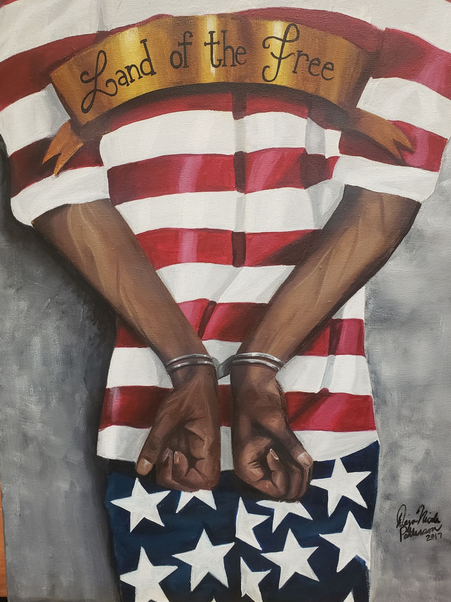 Painting of a handcuffed person from the back wearing a red and white striped shirt and pants with white stars on a blue background. A gold banner over the person's shoulders reads "Land of the Free."