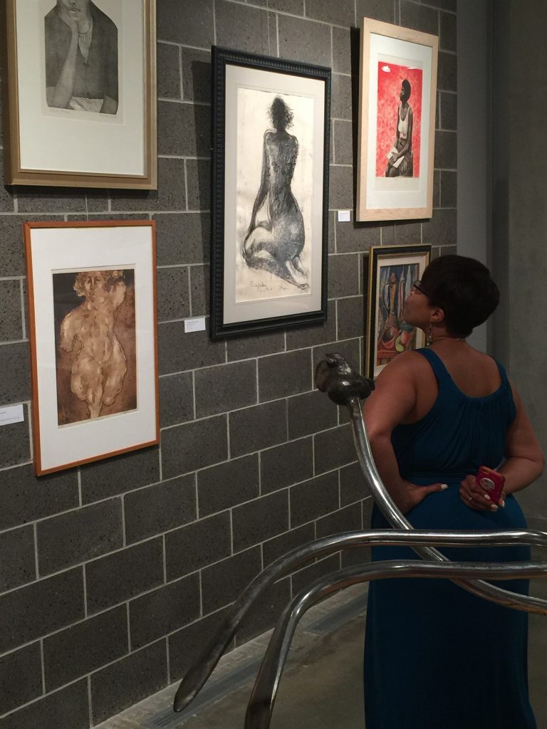 Photograph of Black woman looking at artwork on a gray brick wall