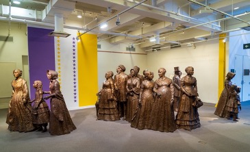Group of bronze statues of men, women and children sited in an indoor space