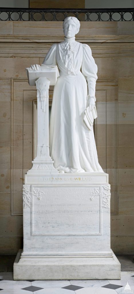 White marble statue of a woman in a long skirt leaning on a lectern