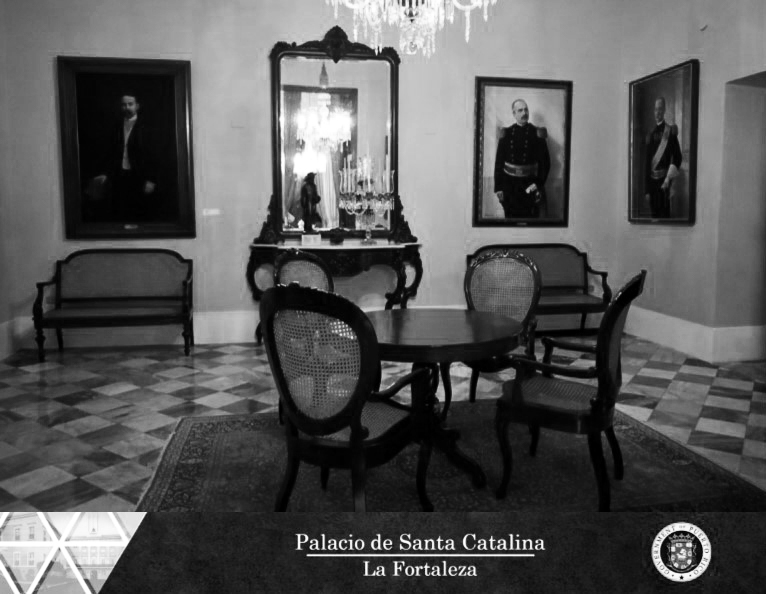 Black-and-white photograph of a formal room with a crystal chandelier and painted portraits on the walls