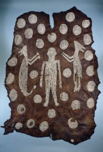 Animal hide with shell decorations in the form of a human figure flanked by animals