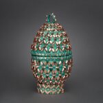 Color photograph of a handmade basketry vessel in shades of blue-green and gold
