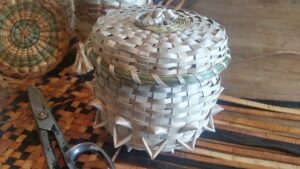 Color photograph of a handmade white basketry vessel, with another basket and a pair of metal shears lying nearby