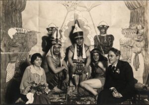 Black-and-white photograph of five people in costume, behind a racist painting of stereotyped African figures