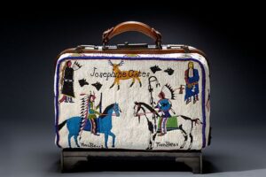 Color photograph of a suitcase with beaded decorations of four Native American figures, a deer, and four silhouettes of wolves' heads. The case is inscribed "Josephine Gates" and two figures on horseback are identified as Two Bear 2 and Two Bear