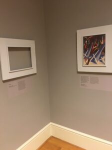 Interior view of a corner of a museum gallery with a work of art on the right side of the corner and an empty frame on the other side