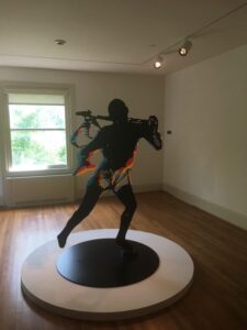 Sculpture inside a room with a wood floor and a window of a man brandishing a weapon 