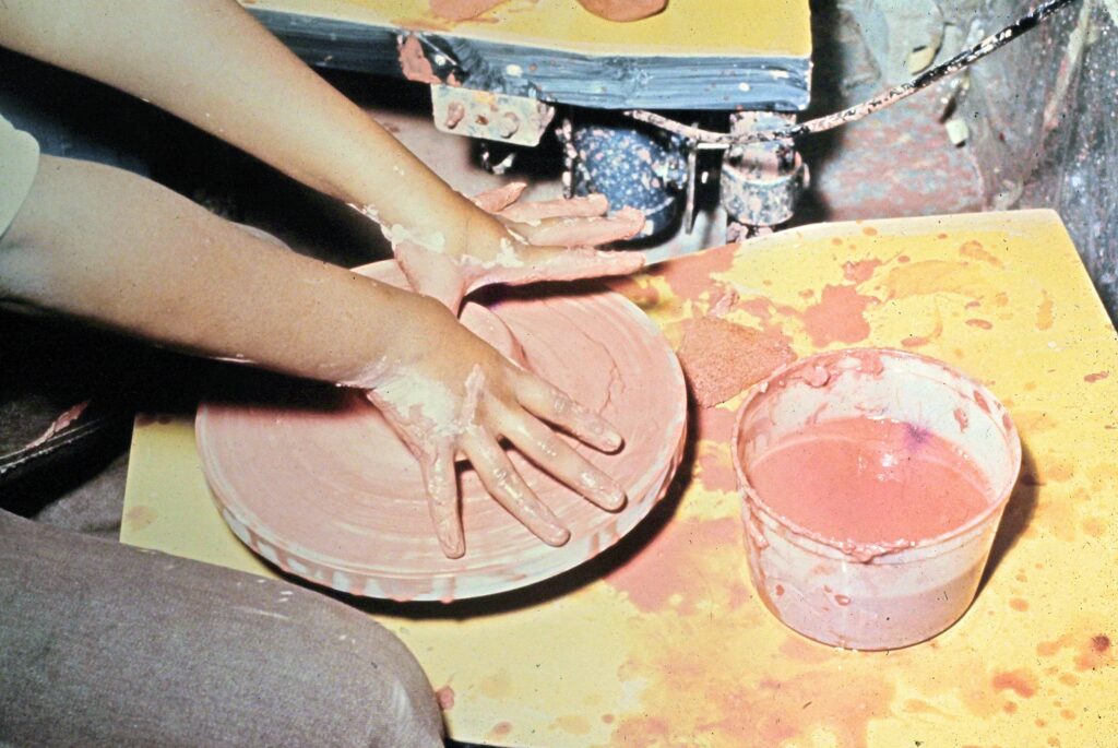 Color photograph of two hands working with clay on a pottery wheel