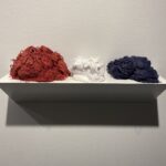 Wall shelf holding three piles of loose thread: red, white, and navy blue