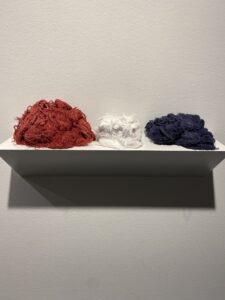 Wall shelf holding three piles of loose thread: red, white, and navy blue