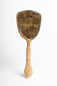 Photograph of a brown and tan hand mirror with the word BREATHE on the back