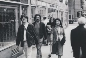 Black-and-white photograph of four people walking together down a city street