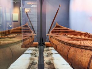 Museum display of two canoes, seen from the back end, with a text panel in front of them.