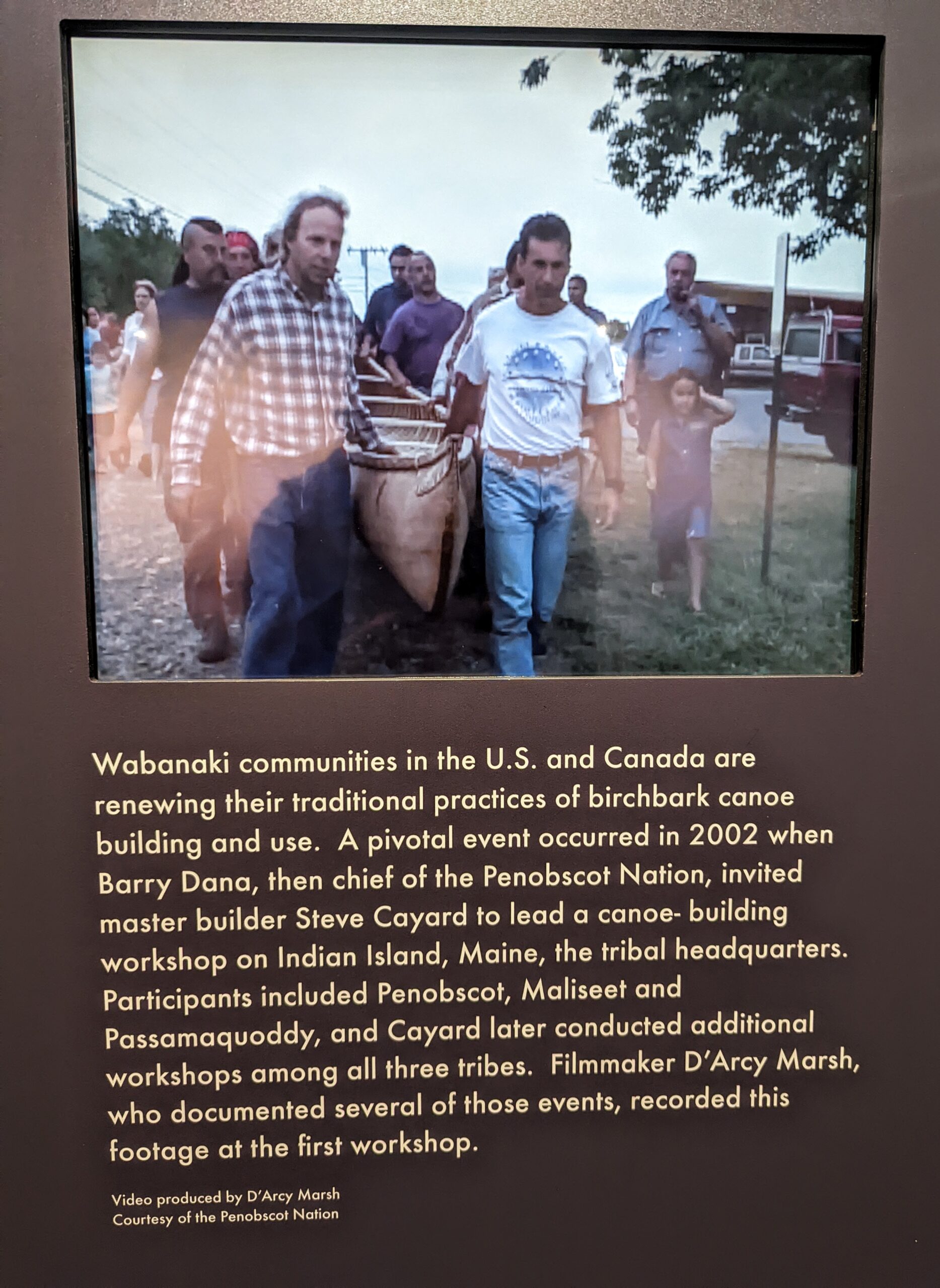 Museum text panel about Wabanaki canoe building, featuring photograph of several men carrying a canoe