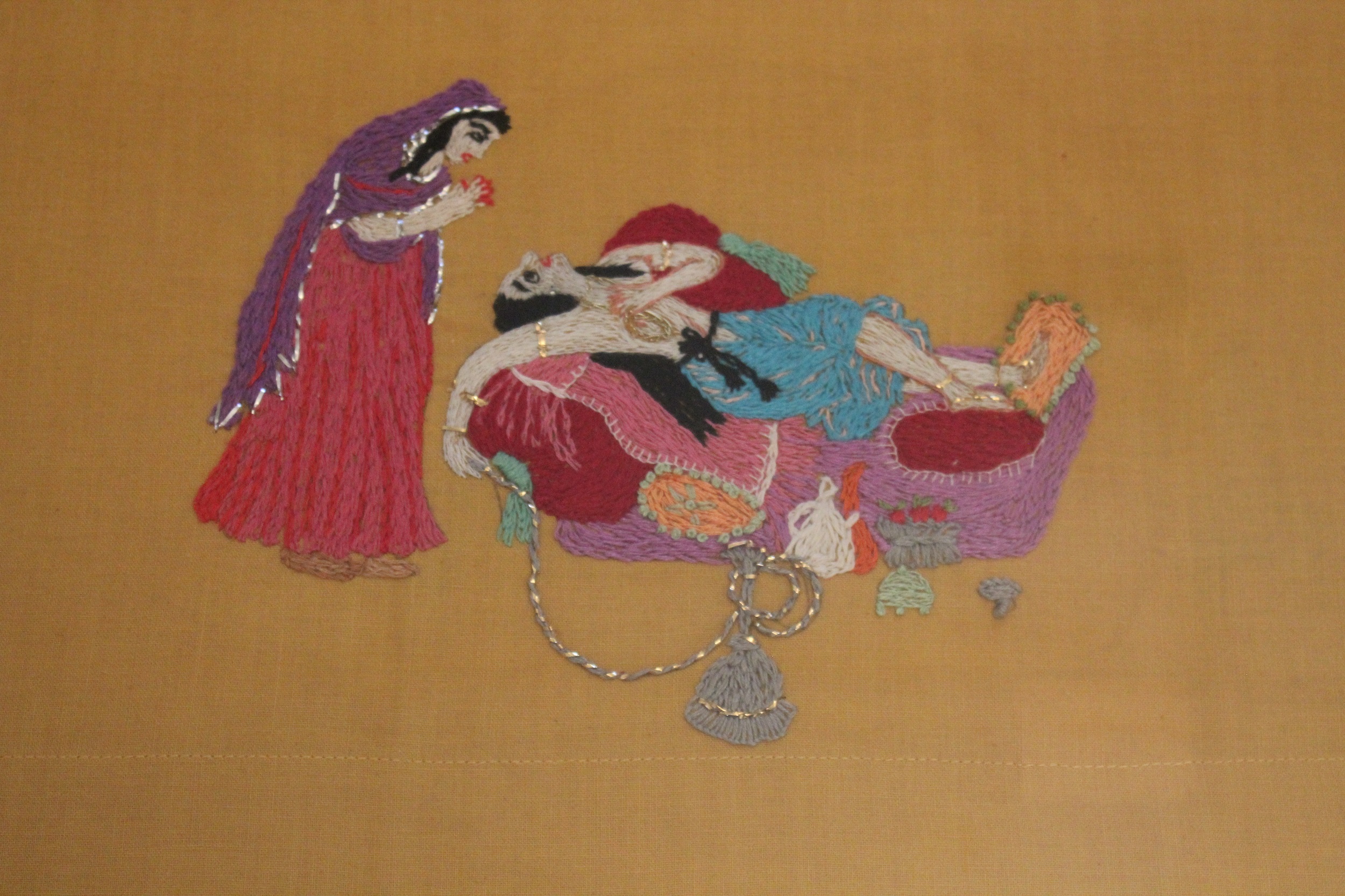 Embroidered scene of a woman in along purple veil bending over another woman lying on a couch with a hookah pipe