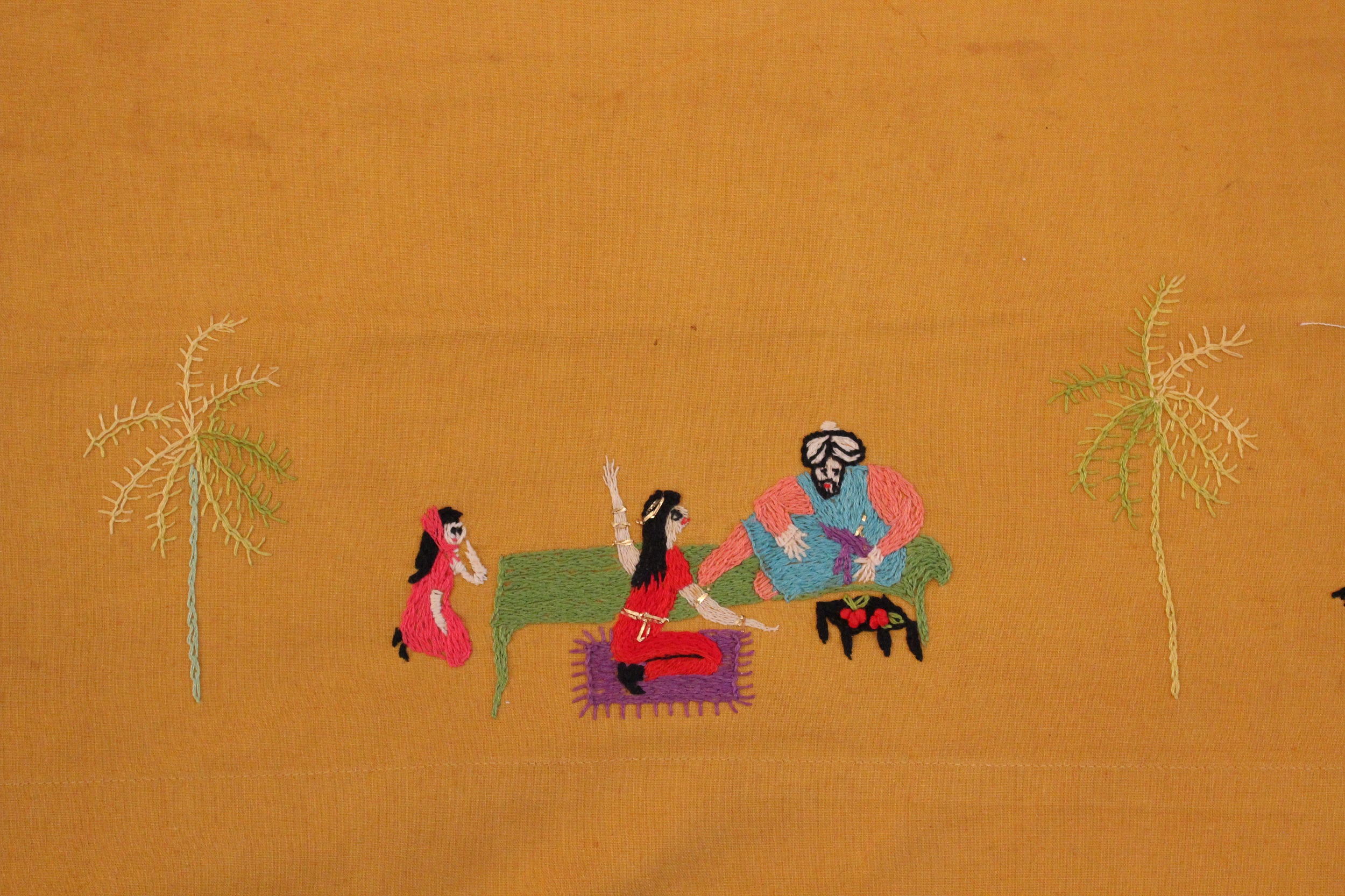 Embroidered scene of a man seated on a low green couch, conversing with two young girls