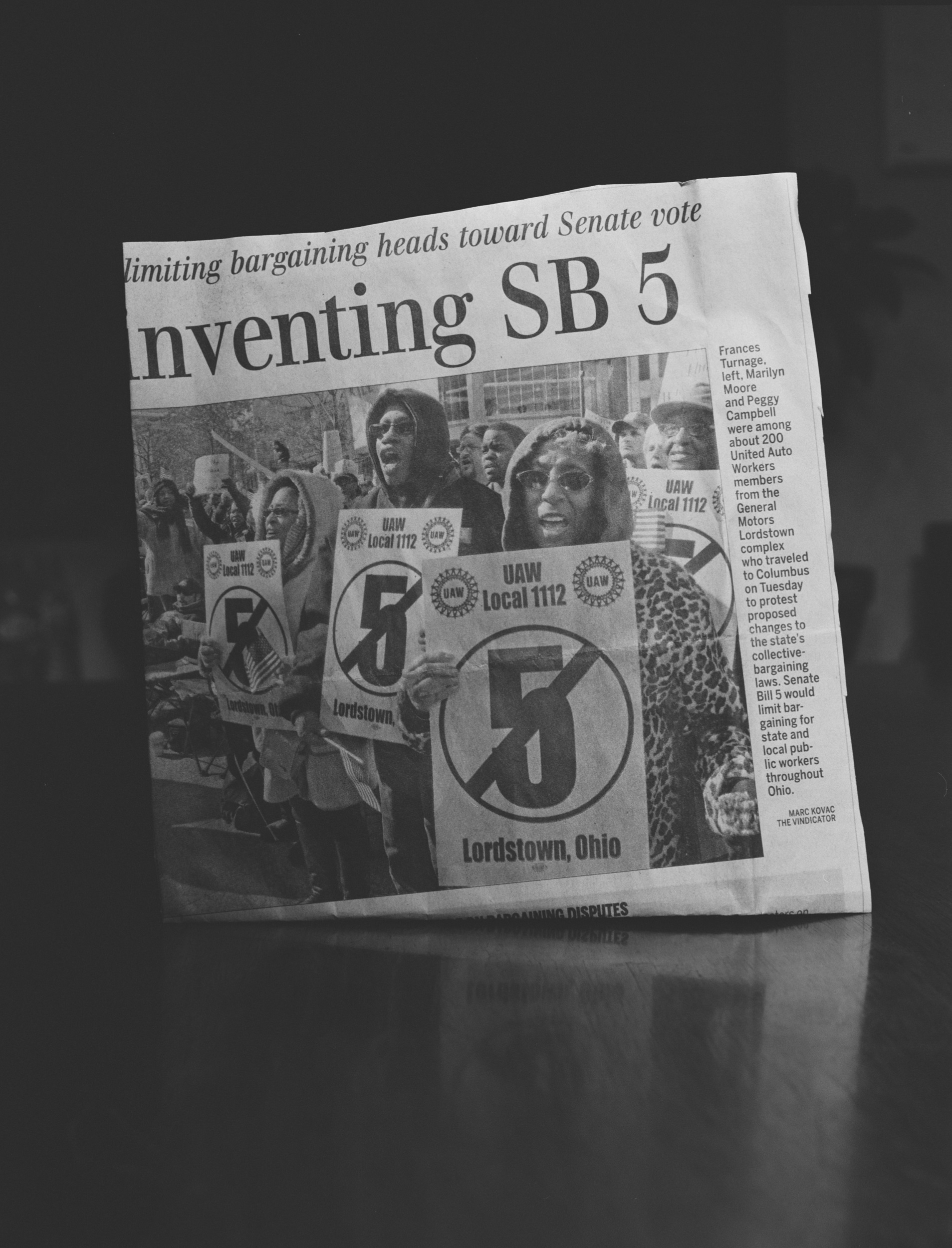 Black-and-white photograph of a newspaper with an image of striking workers in Lordstown, Ohio, under a partial headline reading "...nventing SB 5"