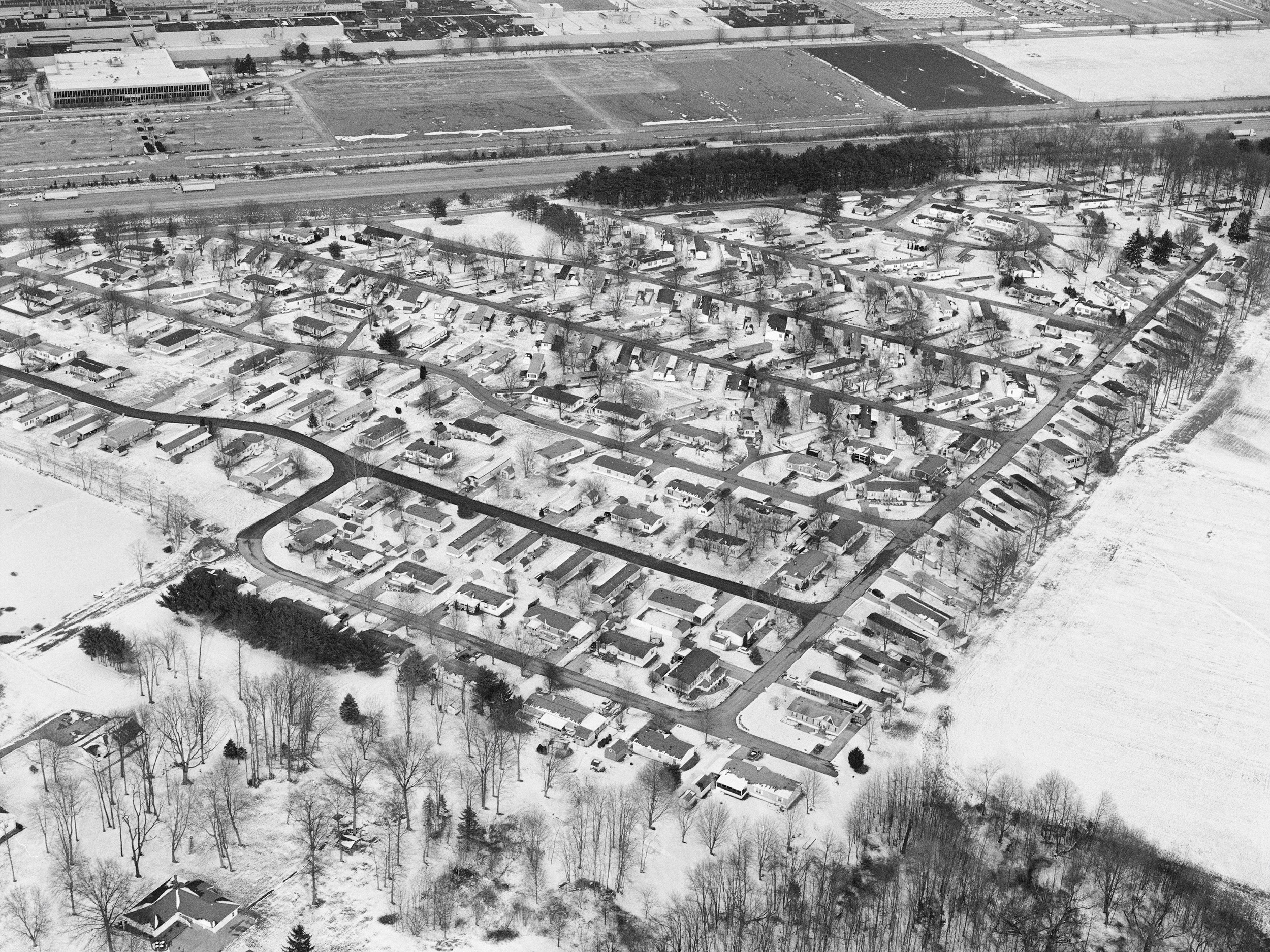Black-and-white aerial photograph of a housing development in winter, across the street from an industrial site