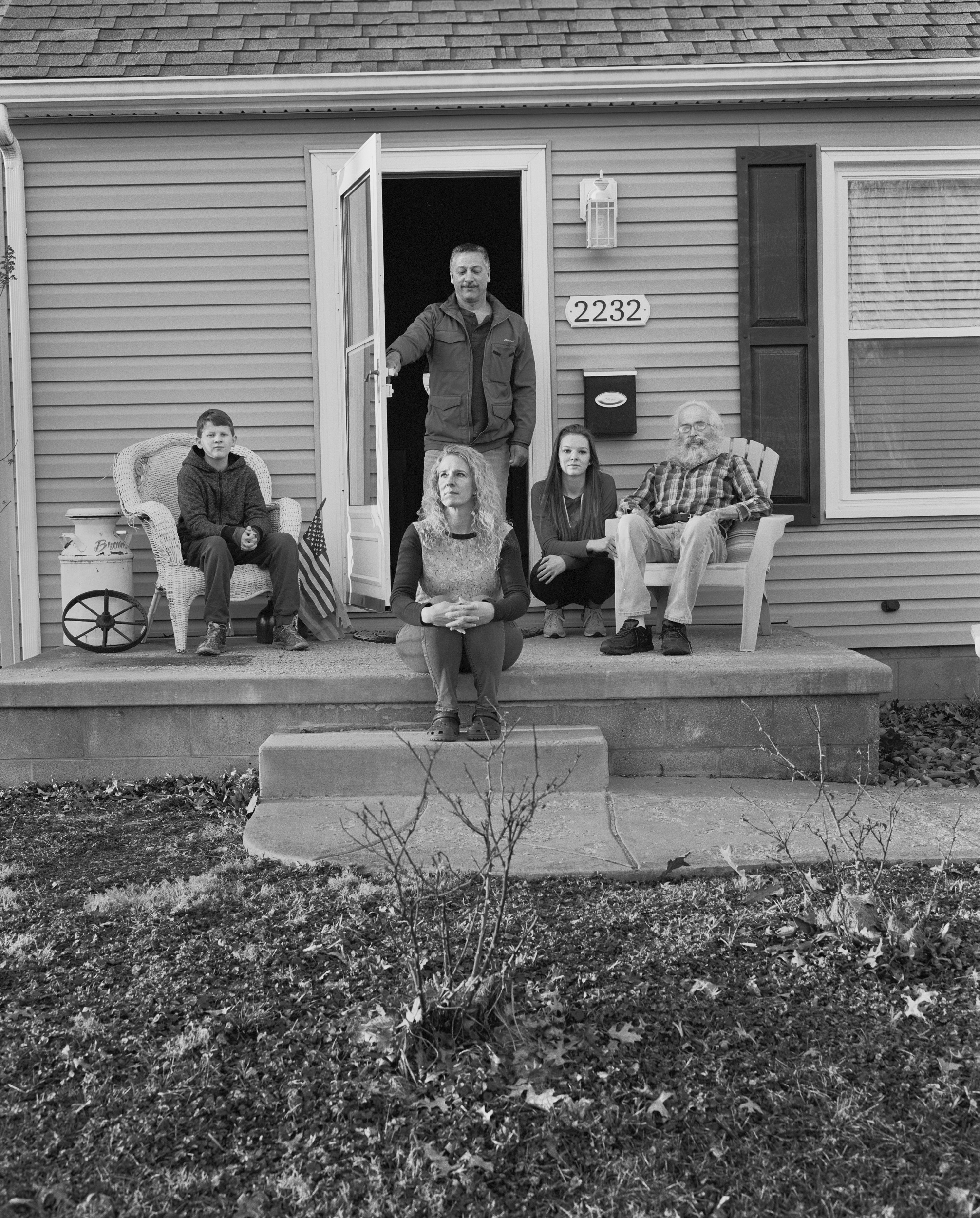 Black-and-white photograph of a white family sitting outside the front door of their small, clapboard home