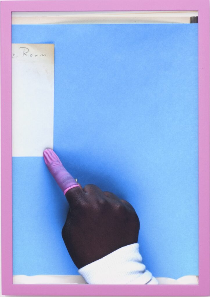 Bird's eye view of a hand with dark skin, a pink rubber sleeve covering one finger, holding a document down on a flatbed scanner