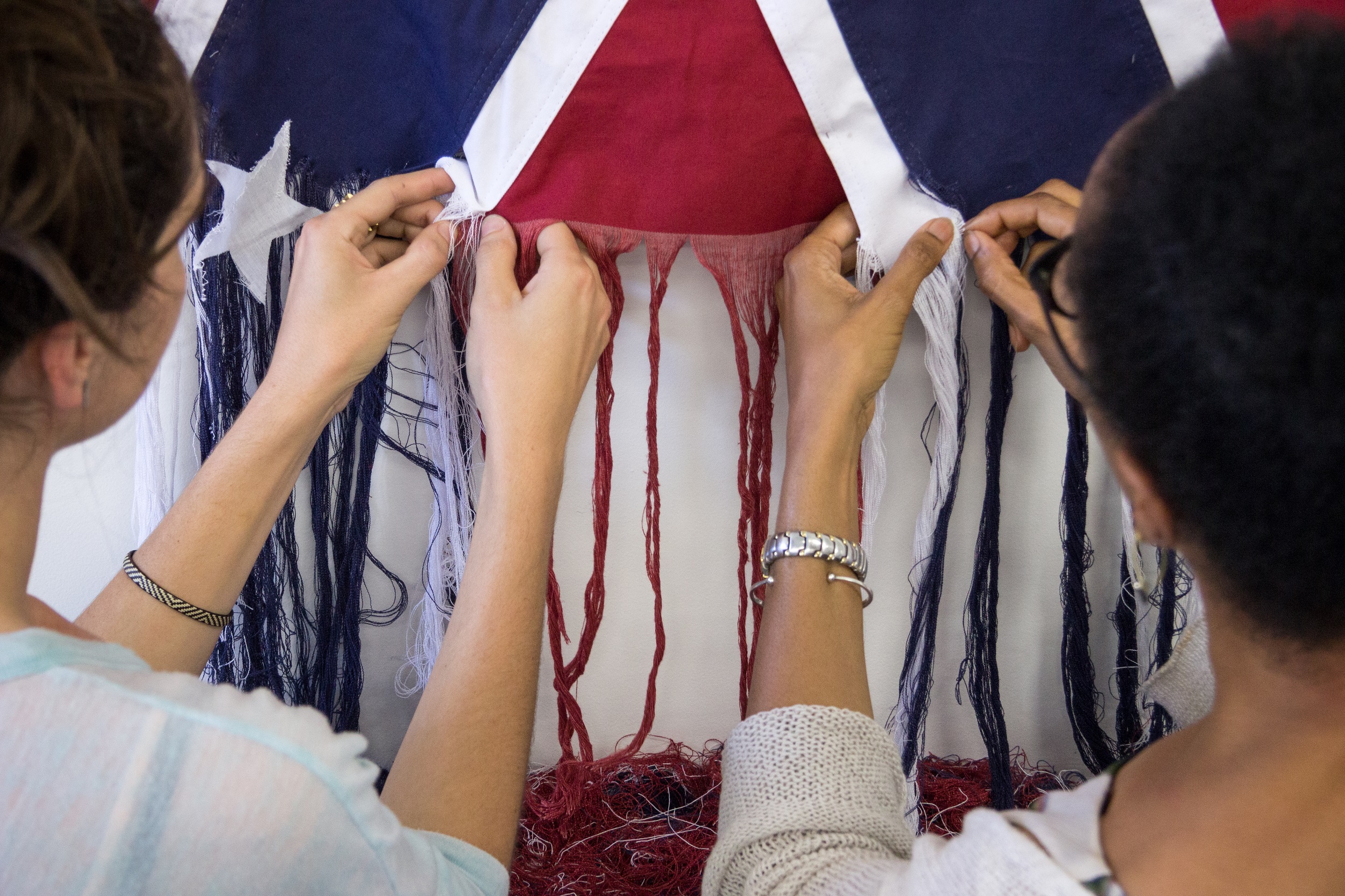 Color photograph of two women carefully unraveling the bottom edge of Confederate battle flag