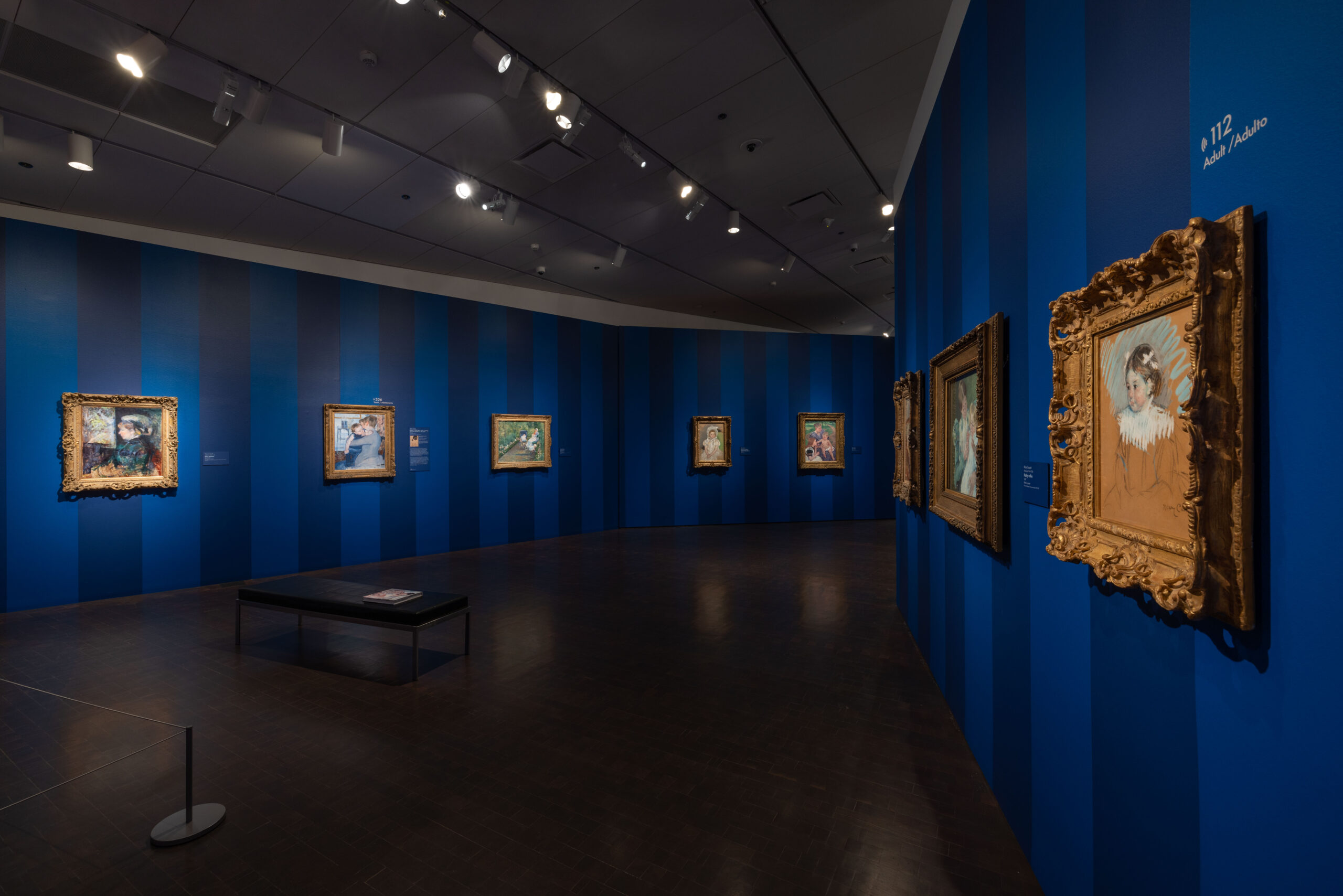 Interior of a museum gallery, the walls painted with wide, deep blue stripes, with eight lavishly framed paintings on the walls.