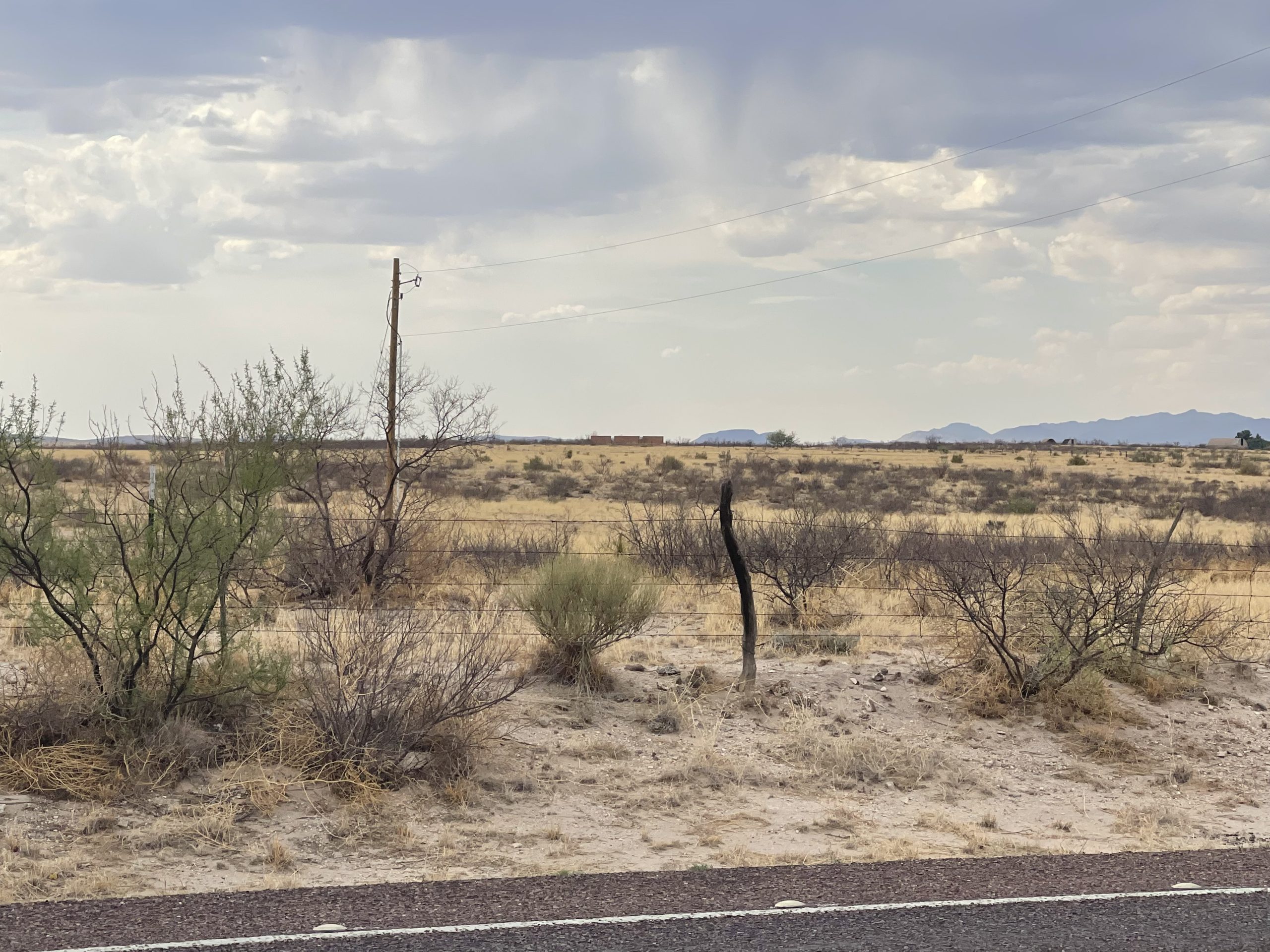 View of a desert landscape with a strip of road in the foreground and a brick wall just visible on the horizon