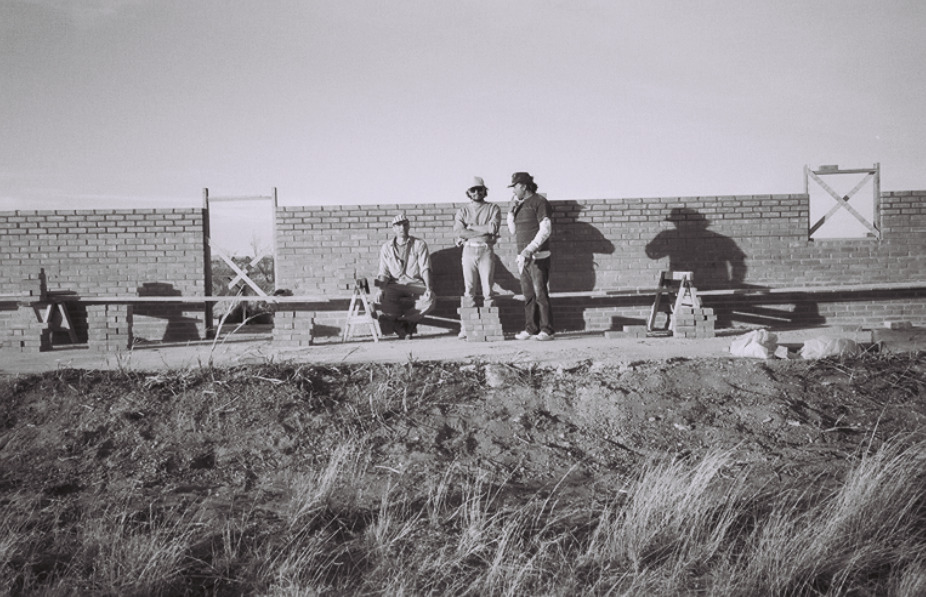 Black-and-white photograph of several workers in front of a low brick wall