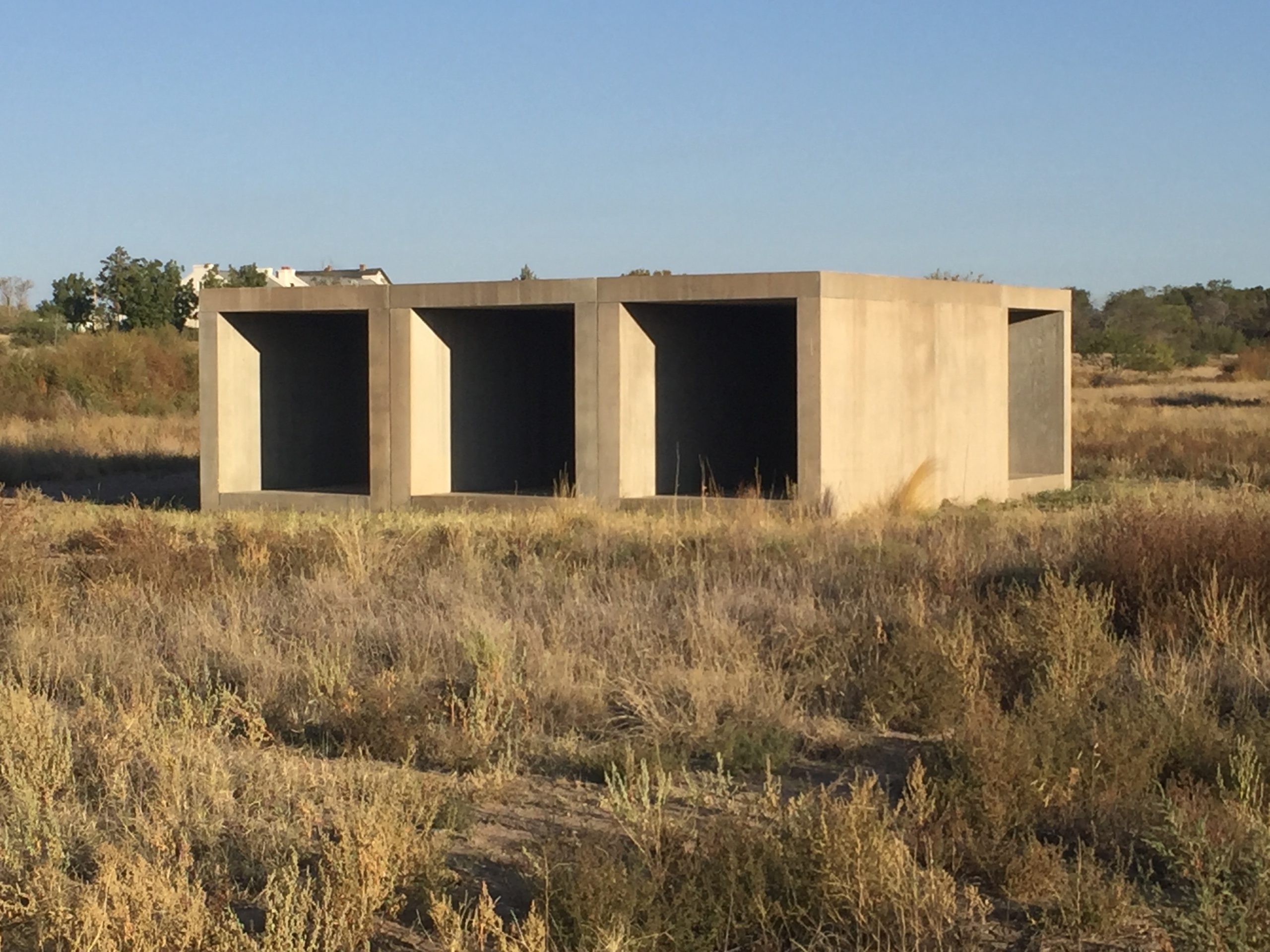 A three-bay concrete structure in a grassy desert setting