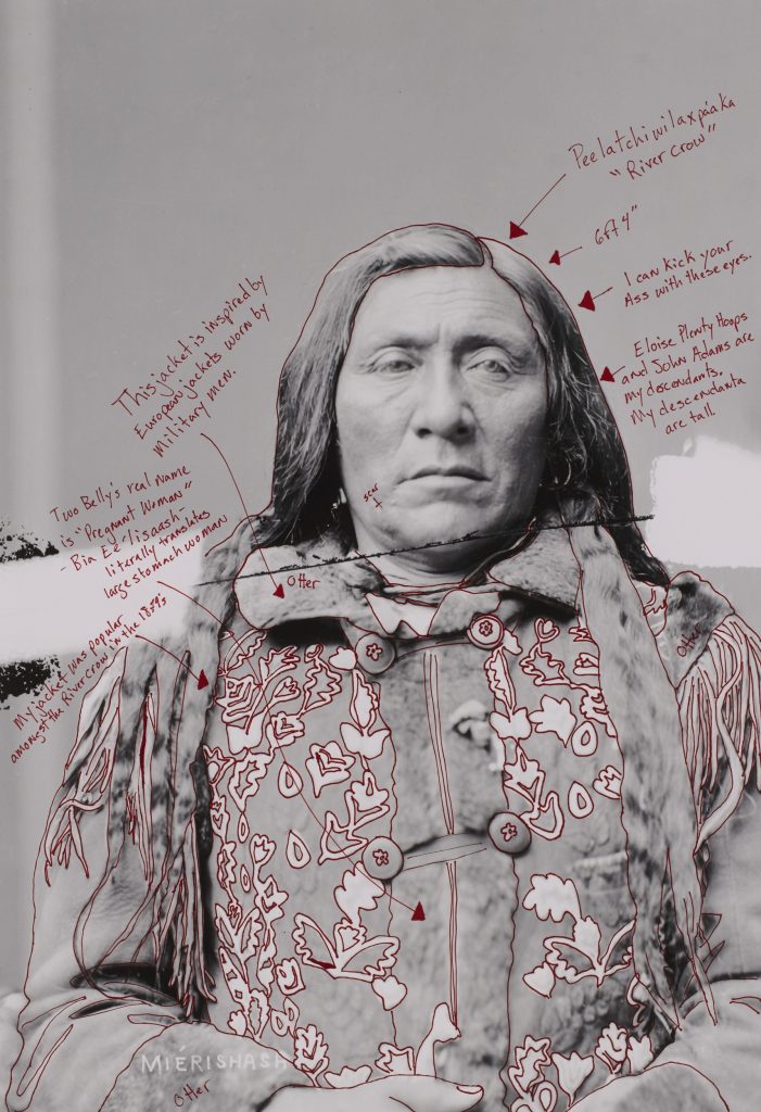 Black-and-white photograph of a Native American individual seen from the waist up. The figure's hair and parts of their costume are outlined in red ink, and various captions in red point out features of the photograph.