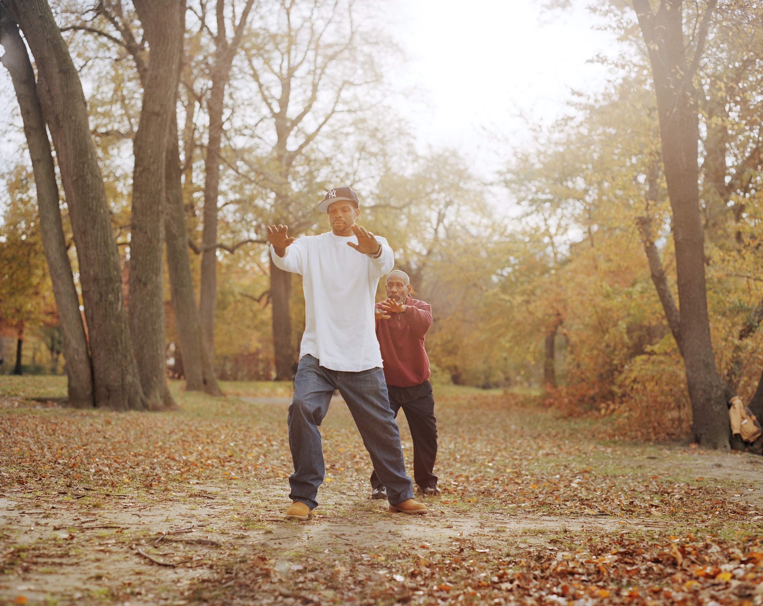 Color photograph of two men practicing T'ai Chi in a wooded, autumnal landscape