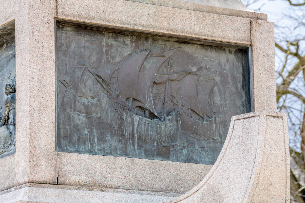 Bronze relief sculpture showing three tall-masted ships in the ocean.