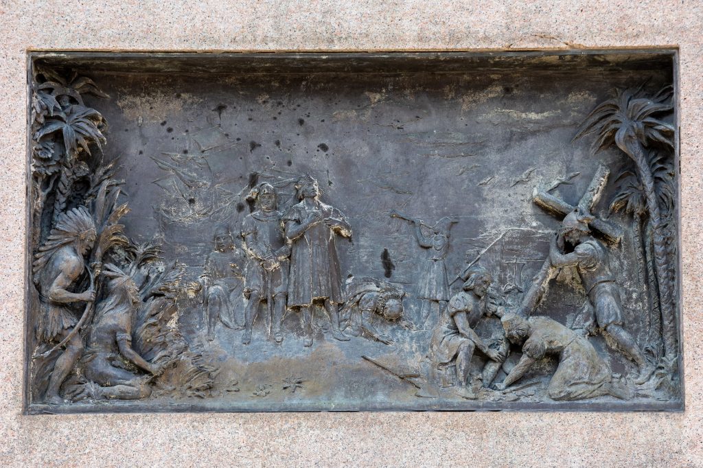 Bronze relief sculpture showing Columbus and his crew coming ashore. To the left are stereotypically depicted native Americans and tropical vegetation; to the right European figures erect a cross.