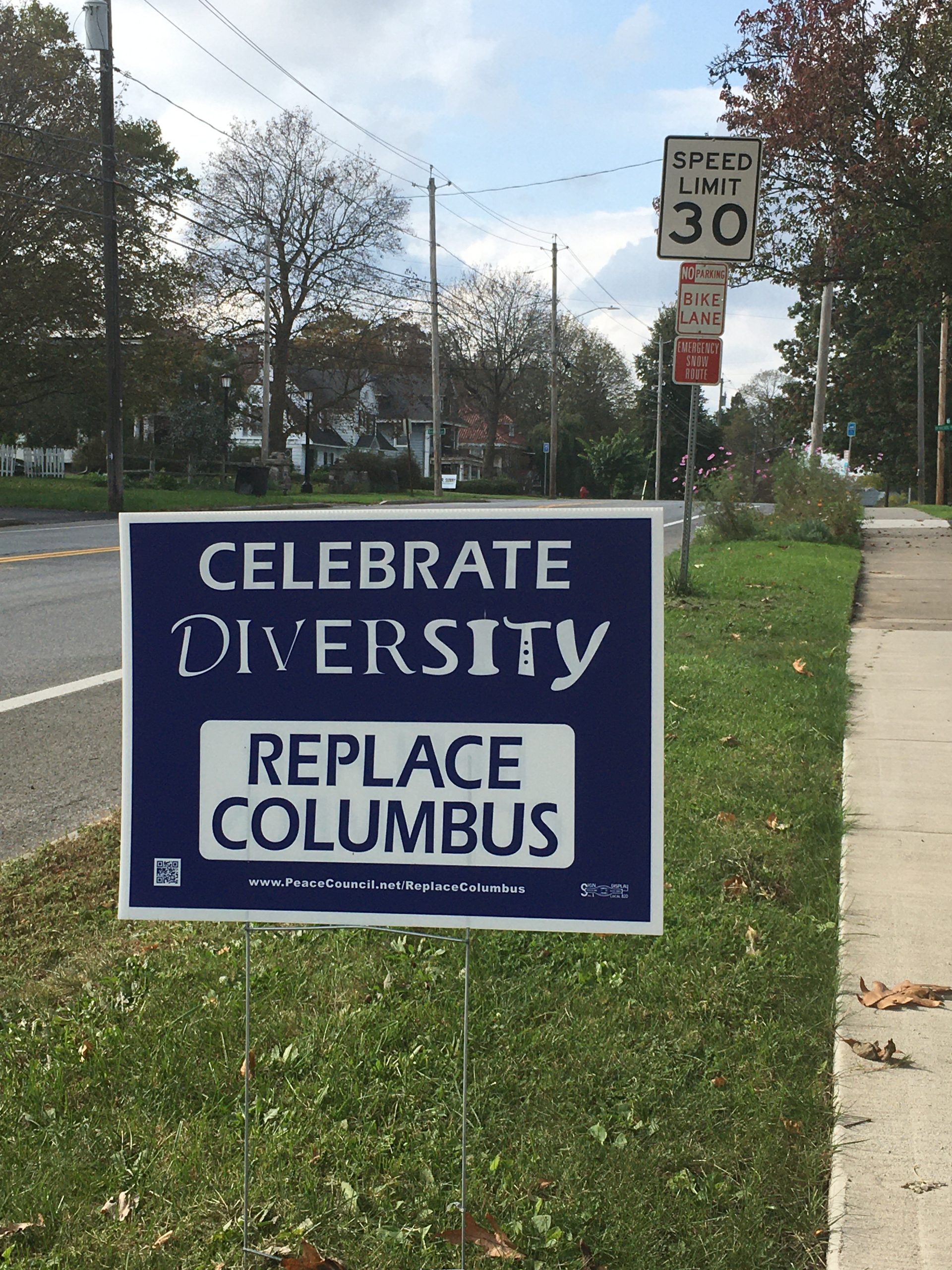 Lawn sign placed on the side of a road reading "CELEBRATE DIVERSITY / REPLACE COLUMBUS"