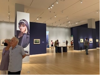 Interior view of a museum gallery, with a large reproduction of a portrait of a woman on the far left