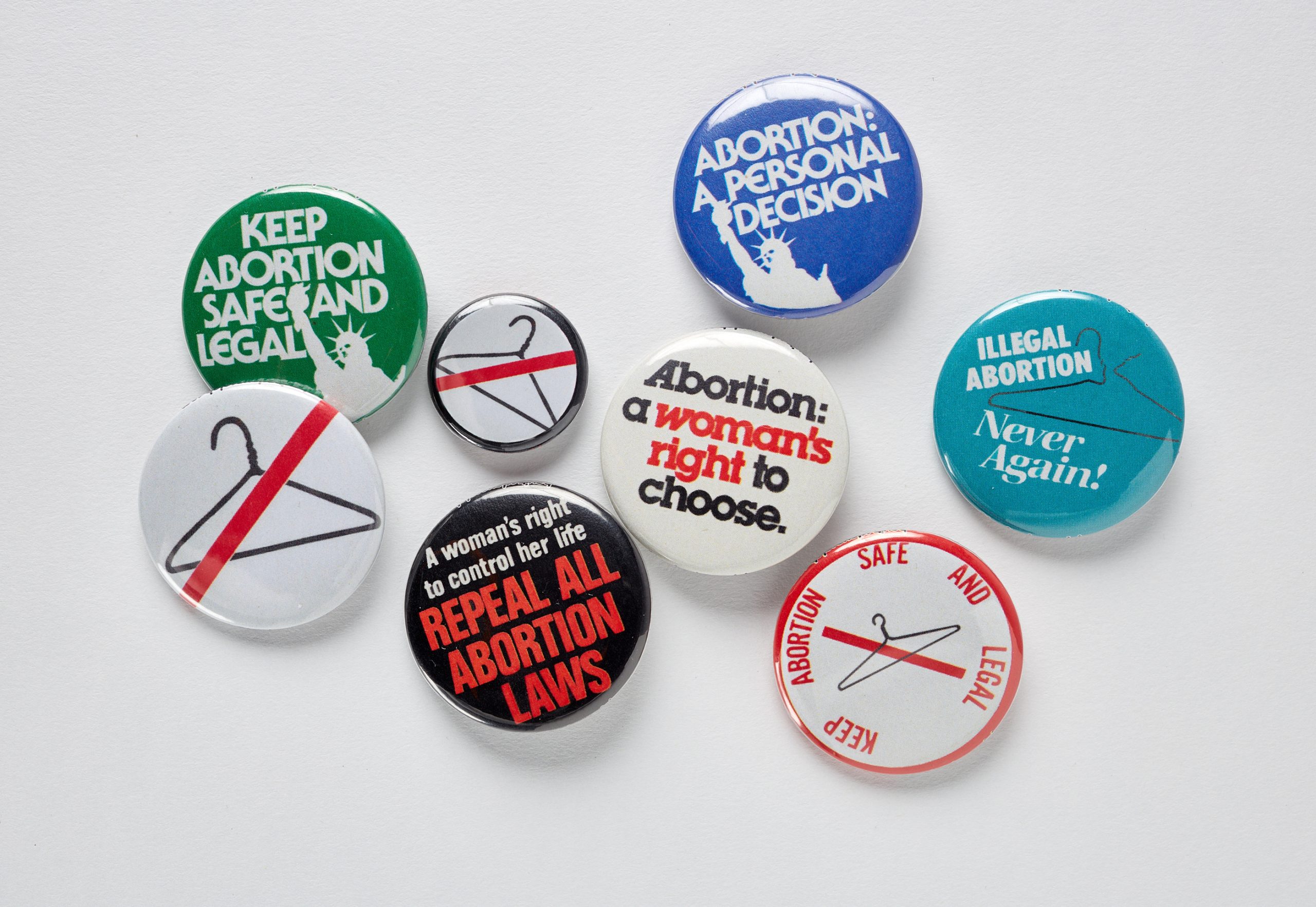 A selection of reproductive rights buttons, featuring the slogans "KEEP ABORTION SAFE AND LEGAL," "ABORTION: A PERSONAL DECISION," Abortion: a woman's right to choose," "ILLEGAL ABORTION: Never Again!" and "A woman's right to control her life: REPEAL ALL ABORTION LAWS," along with two buttons featuring a coat hanger with a diagonal red slash across it.
