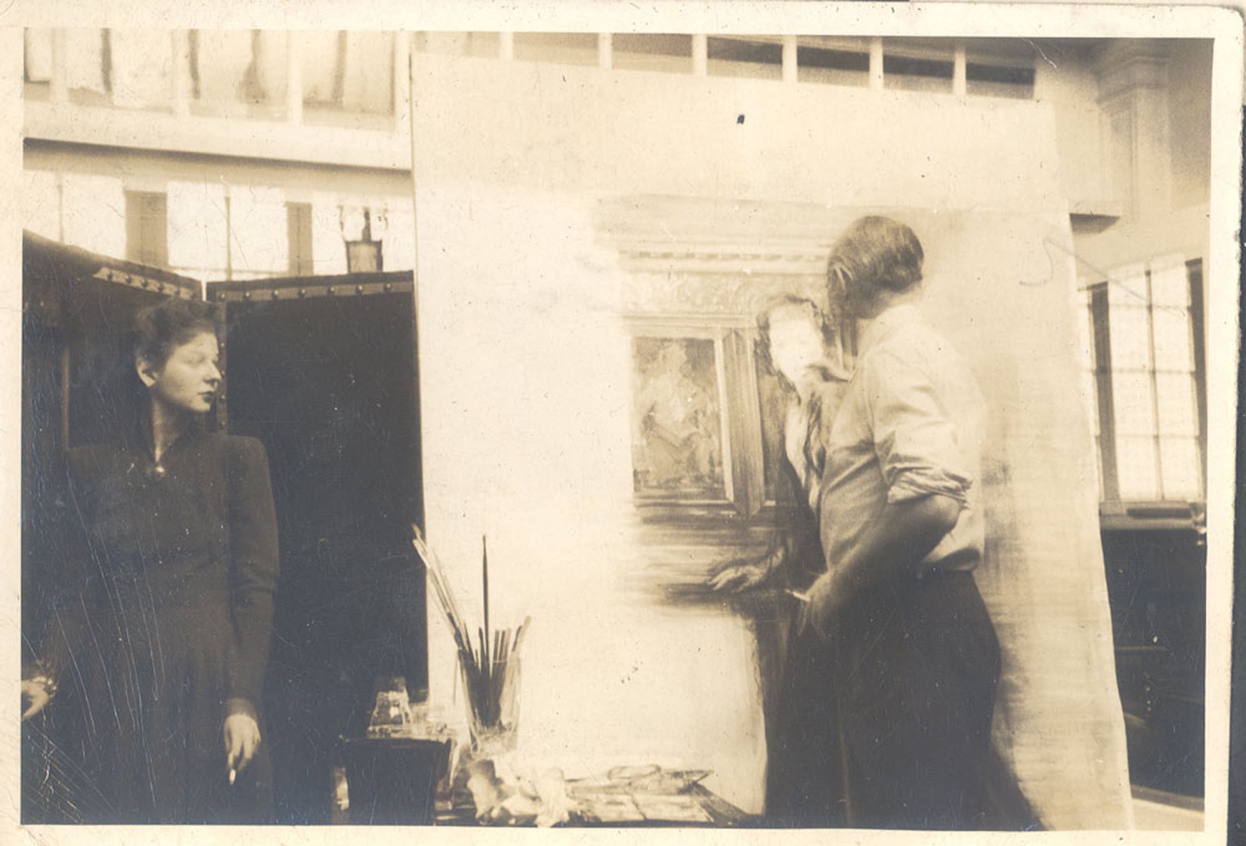 Black and white photograph of a male artist in front of a large canvas, painting the woman who stands to the left.